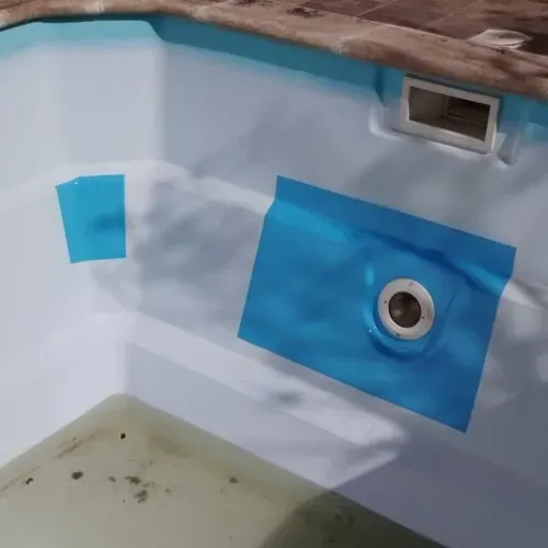Zonas marcadas con cinta azul dentro de una piscina blanca, una alrededor de una lámpara. El agua del fondo está descolorida.