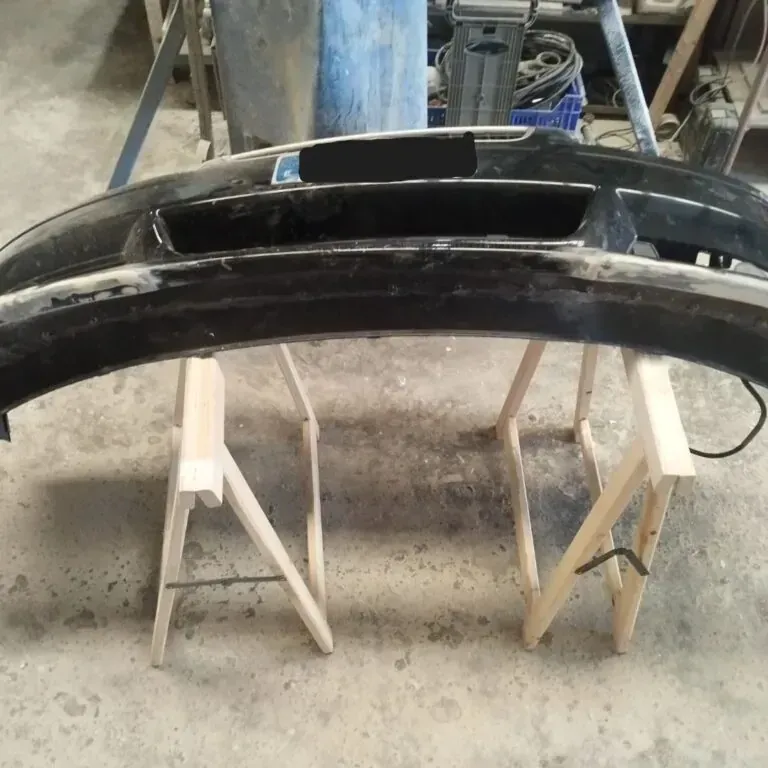 Parachoques de coche negro sobre dos caballetes de madera en un taller.