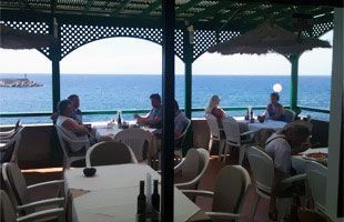 Un grupo de personas están sentadas en mesas en un restaurante con vista al océano.