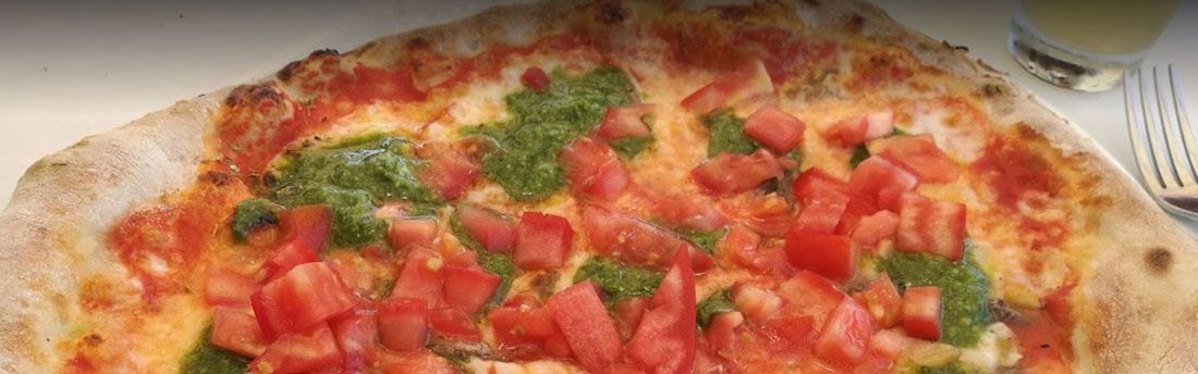 Una pizza con tomates y albahaca está sobre una mesa con un tenedor.
