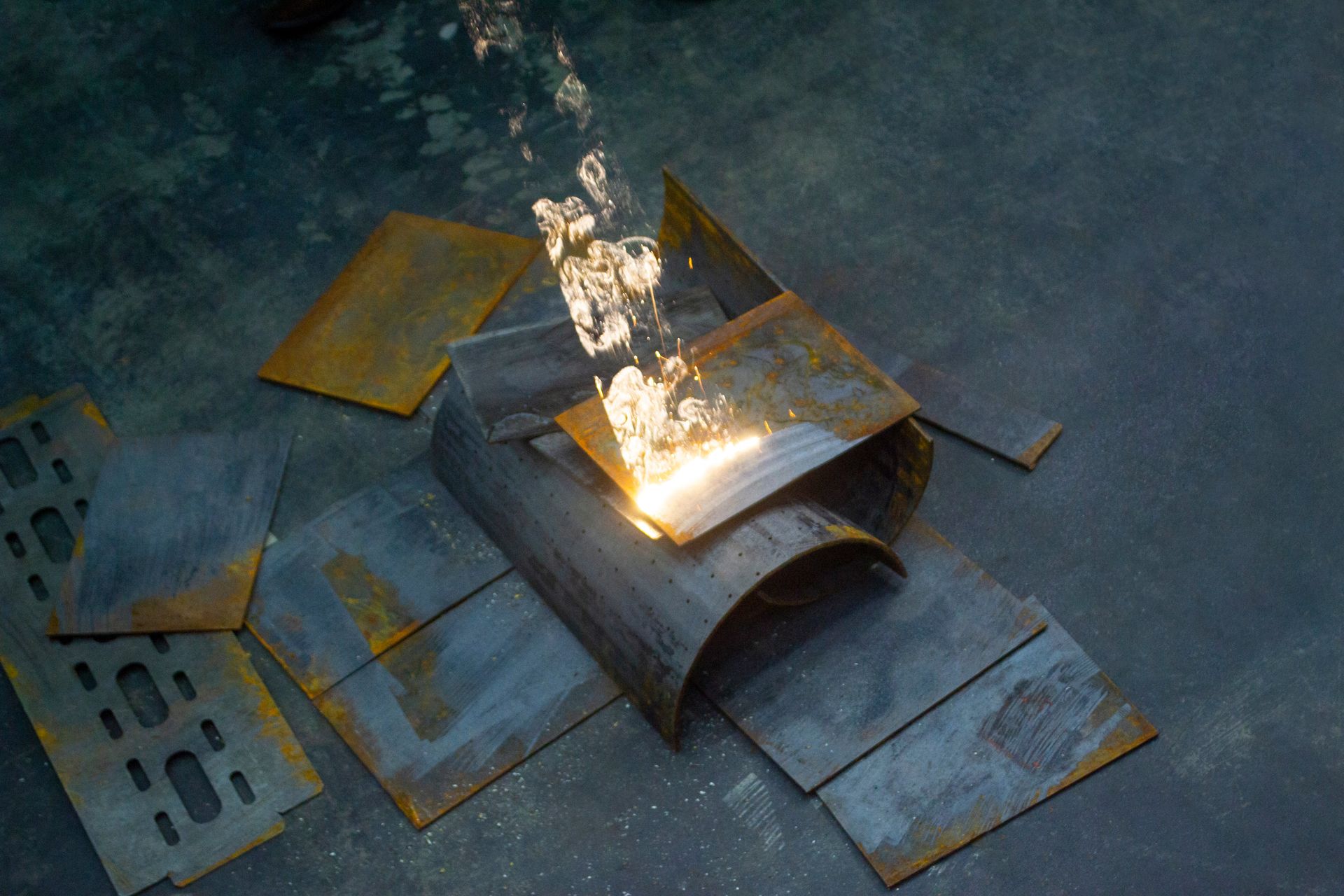 Metall wird mit einer hellen Flamme geschnitten, Funken fliegen. Stahlplatten liegen verstreut auf dem Boden.