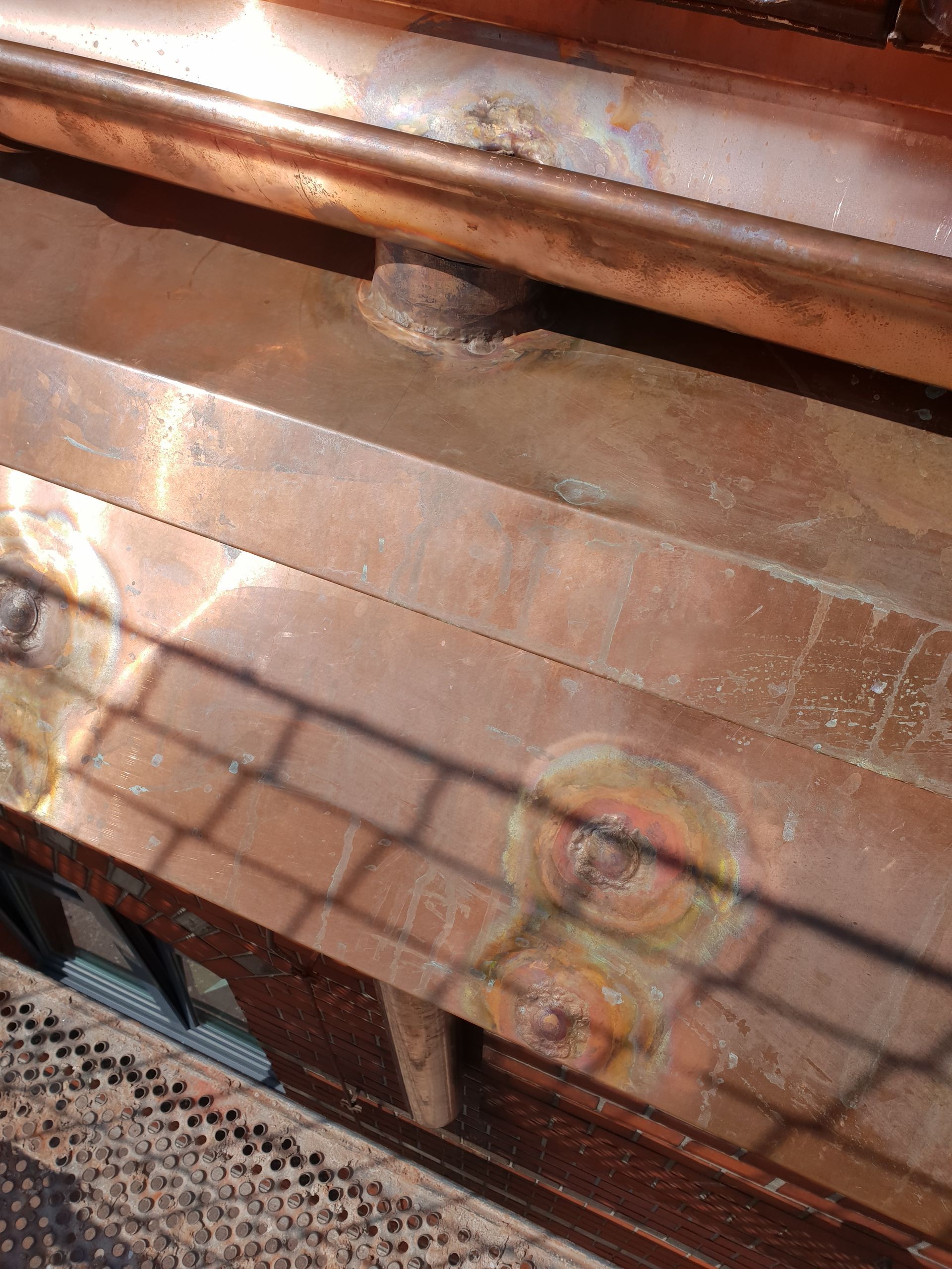 Nahaufnahme von rostbraunem Metall und einem Maschendrahtzaun, wobei das Sonnenlicht Gitterschatten wirft.