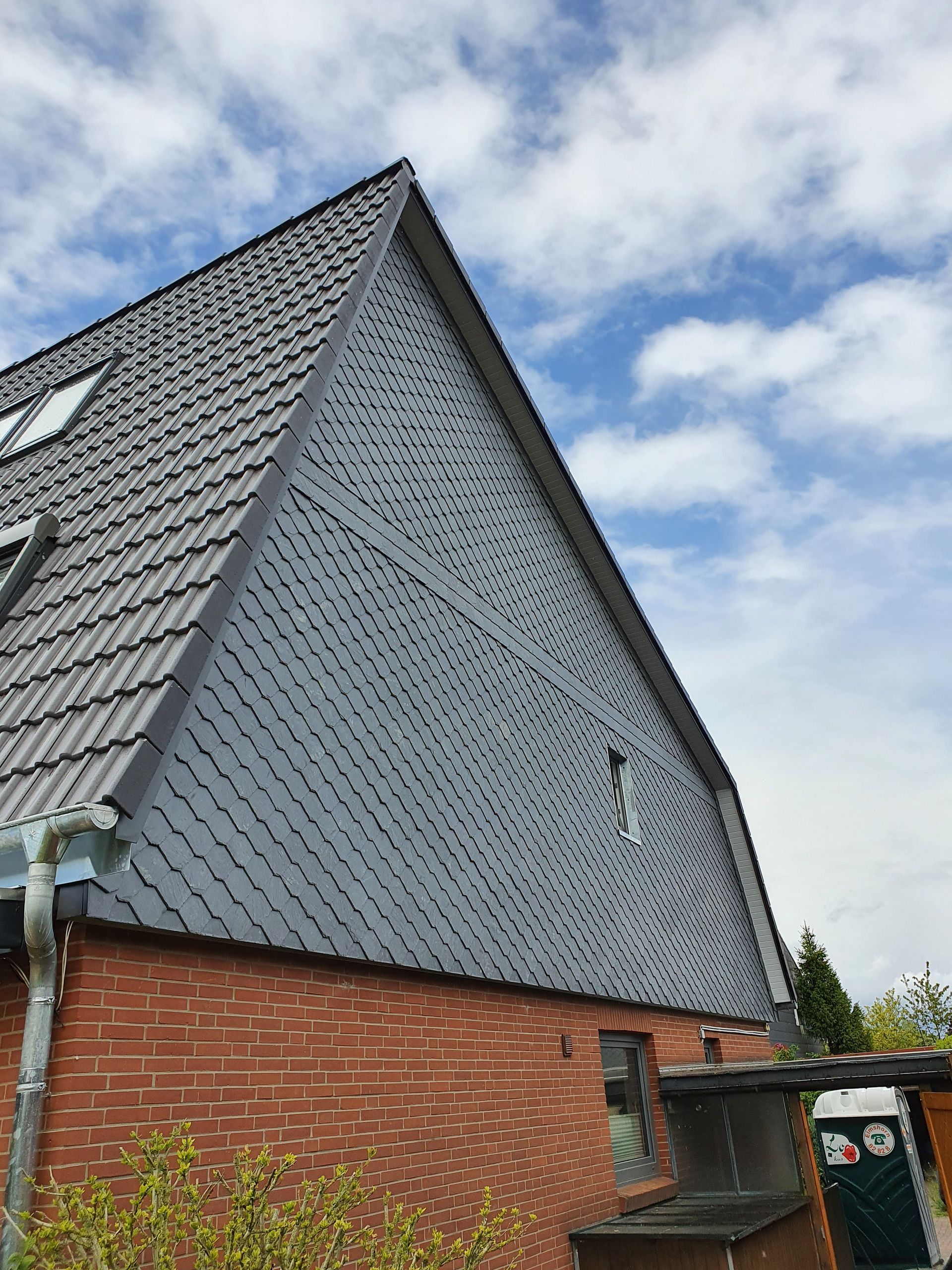 Backsteinhaus mit steilem, grauem Schindeldach unter einem bewölkten Himmel