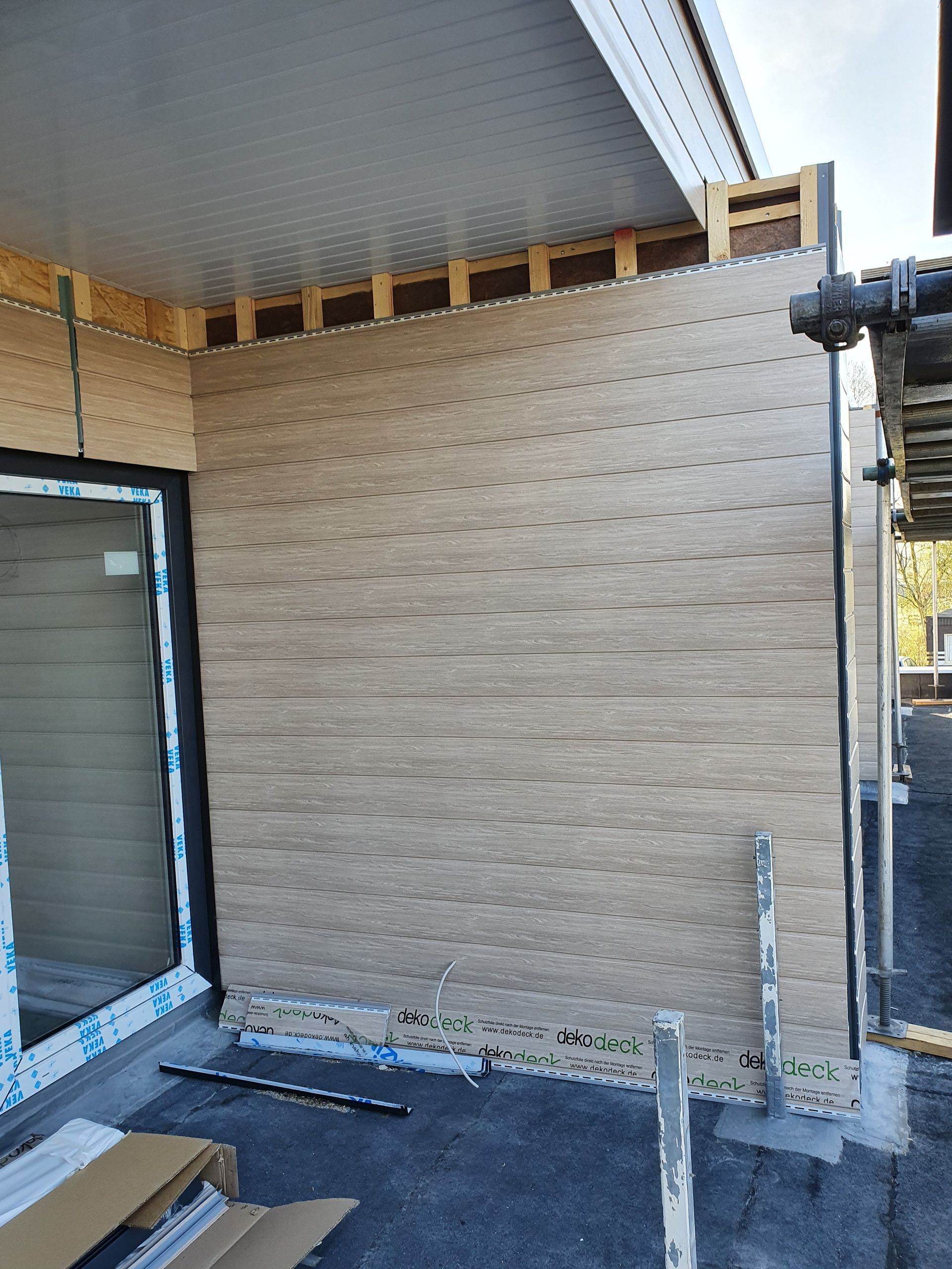 Außenwand im Bau mit beigefarbenen Dämmplatten, einem Fenster und einem Gerüst auf der rechten Seite.
