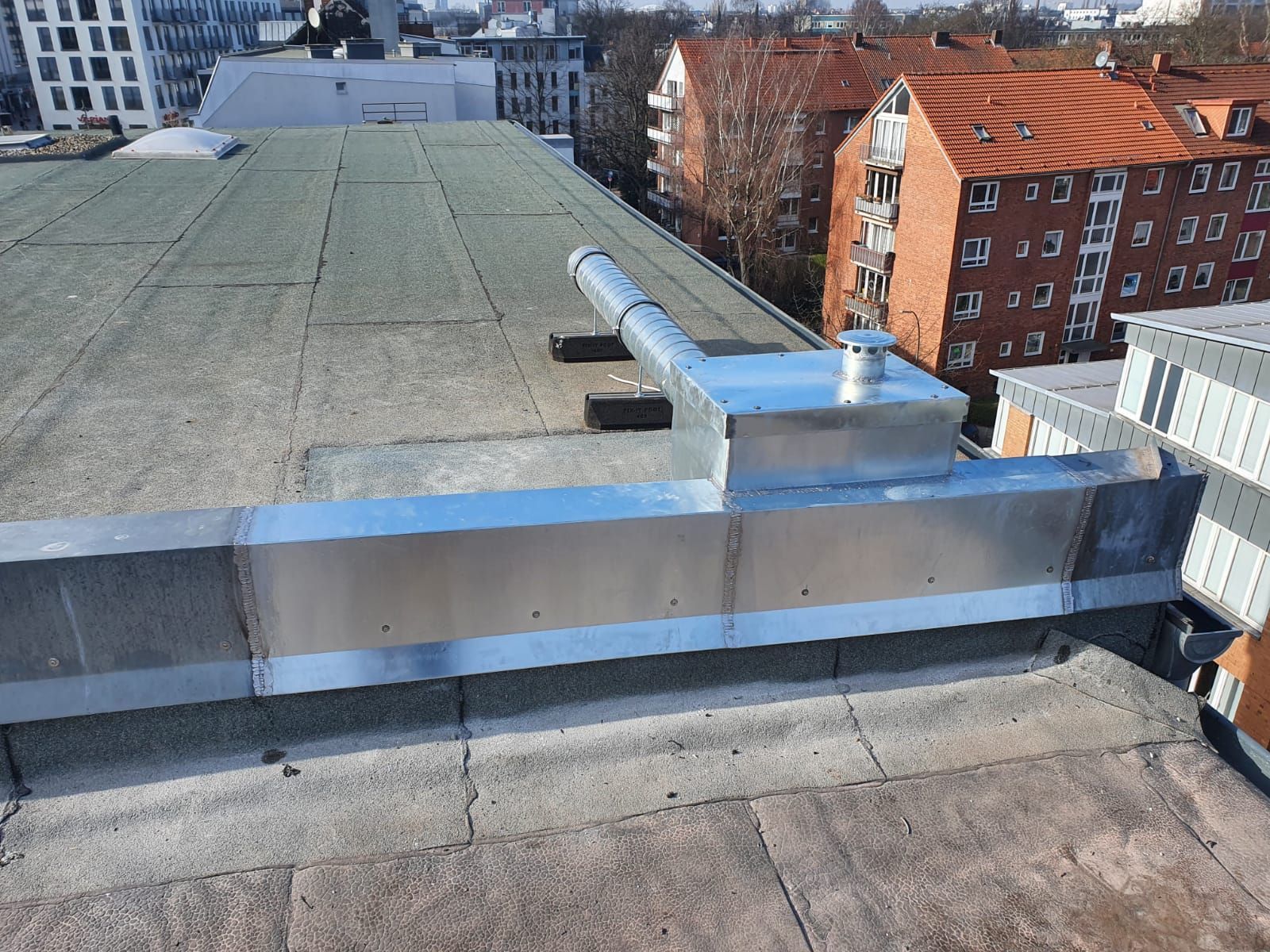 Dach mit Metallbrüstung, grauer Oberfläche und den umliegenden Stadtgebäuden im Tageslicht