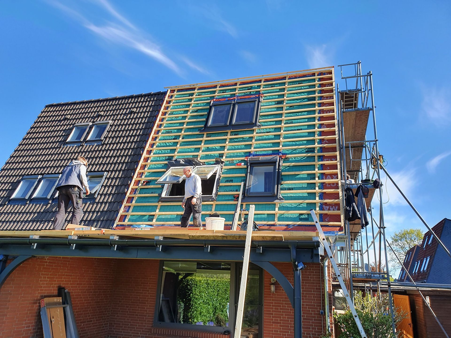 Arbeiter auf einem im Bau befindlichen Hausdach, Dachstuhl und Gerüst vor blauem Himmel.