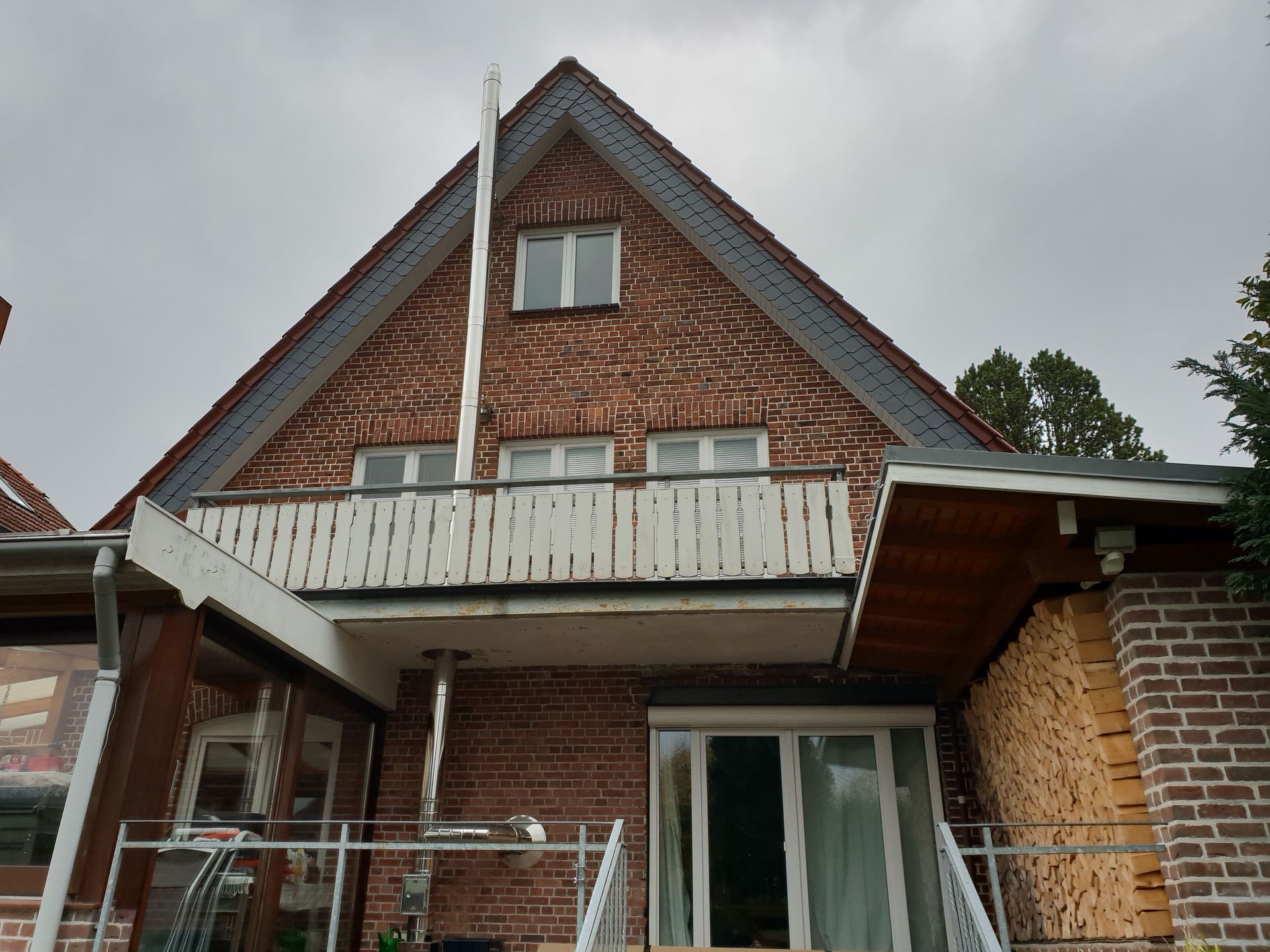 Backsteinhaus mit steilem Giebeldach, weißem Balkongeländer und bewölktem Himmel