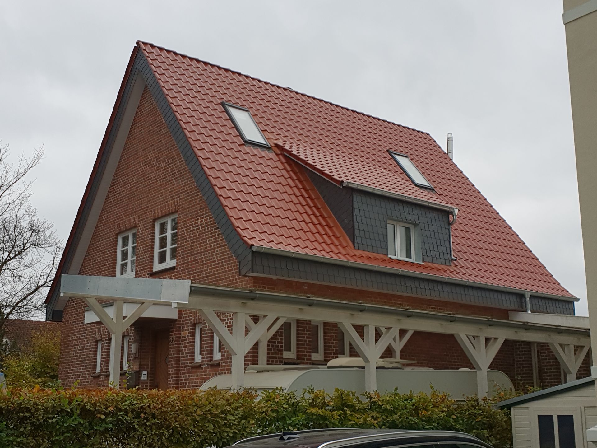 Ein rotes Backsteinhaus mit rotem Ziegeldach und weißen Holzstützen, von der Seite in bewölktem Himmel gesehen.