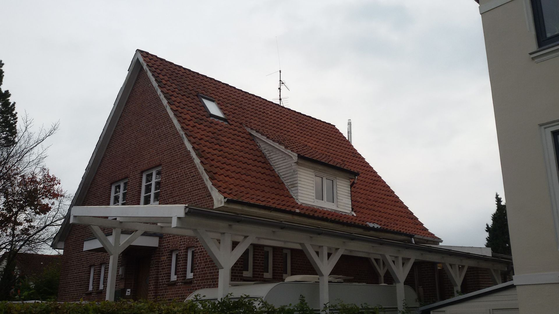 Haus mit rotem Dach und weißer Holzveranda unter bedecktem Himmel