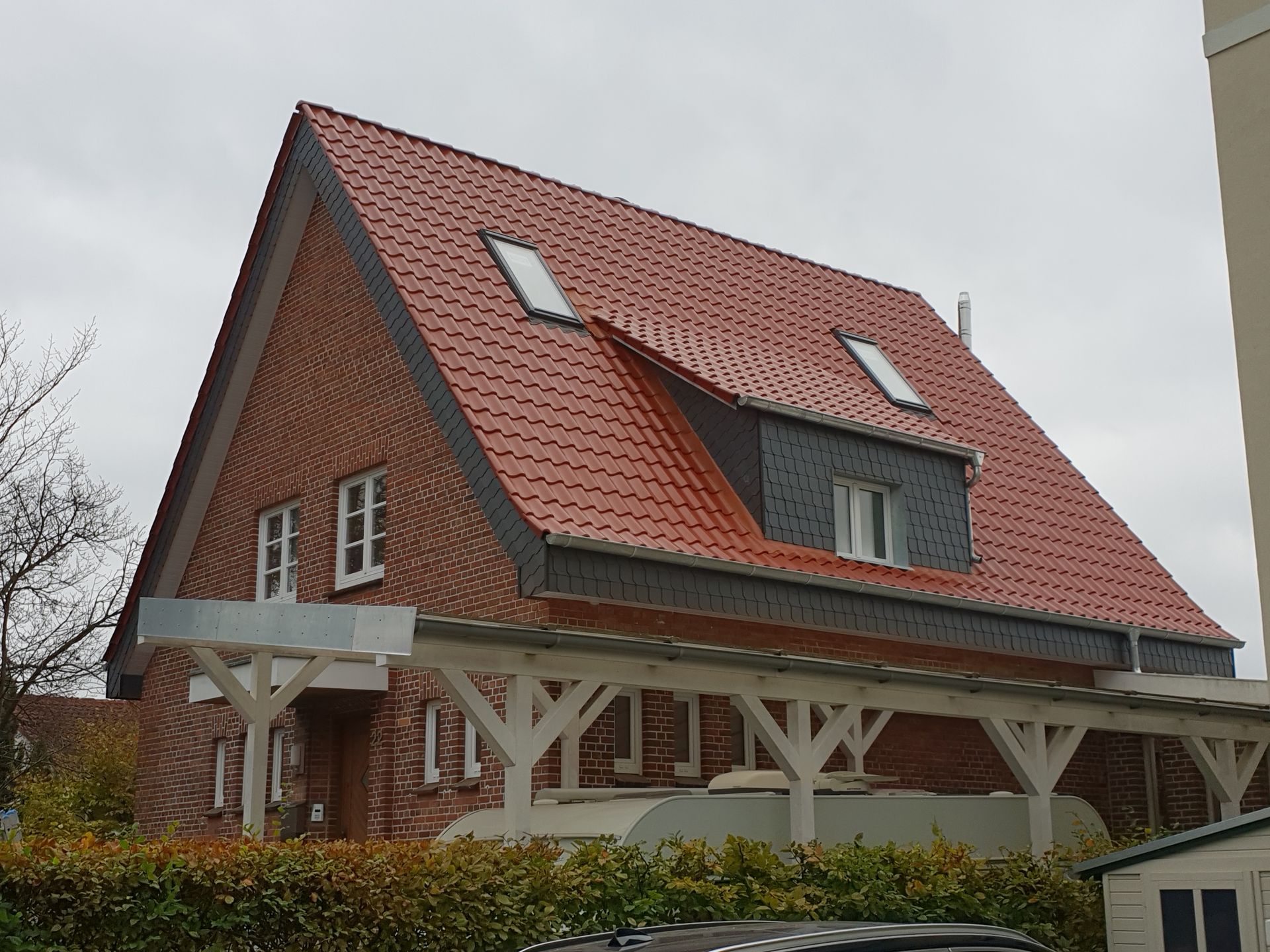 Rotes Backsteinhaus mit steilem, rot gedecktem Dach und weißer Holzveranda in ländlicher Lage