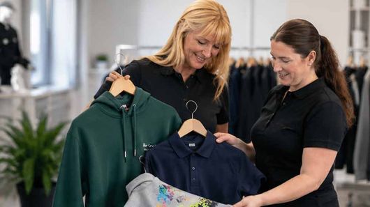 Zwei Frauen vergleichen Kapuzenpullover auf Kleiderbügeln in einem Bekleidungsgeschäft