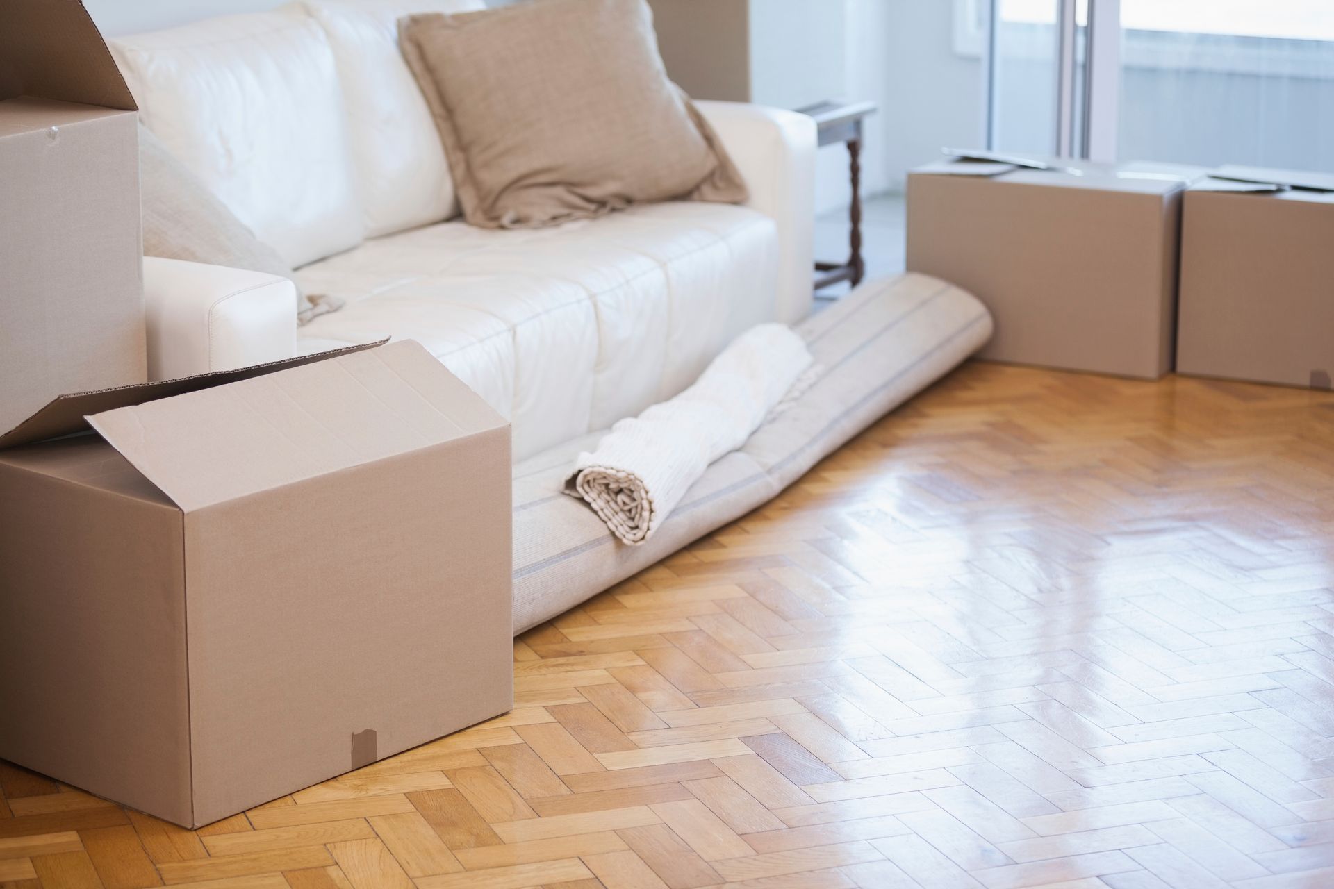 Cajas en habitación con sofá, alfombra enrollada, suelo de madera; día de mudanza.