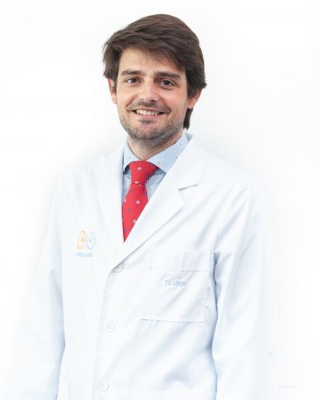 Un hombre con bata blanca y corbata roja está sonriendo.