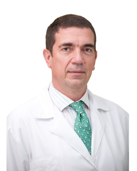 Un hombre con una bata blanca y corbata verde está de pie frente a un fondo blanco.