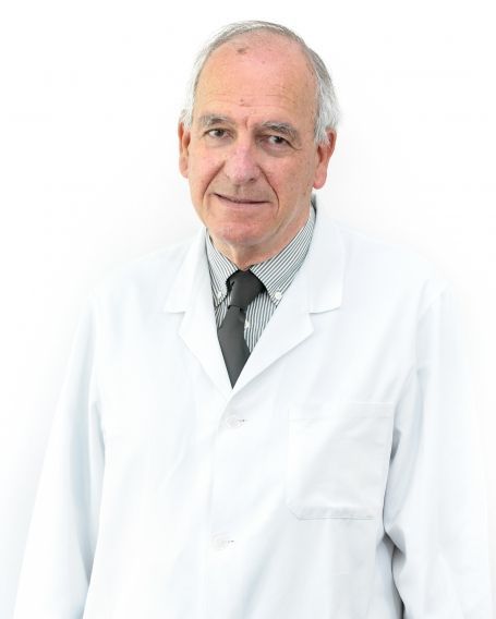 Un hombre con bata blanca y corbata está de pie frente a un fondo blanco.