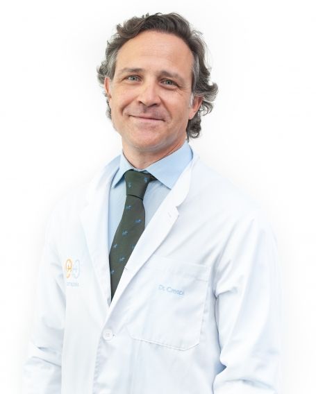 Un hombre con bata de laboratorio y corbata sonríe para la cámara.