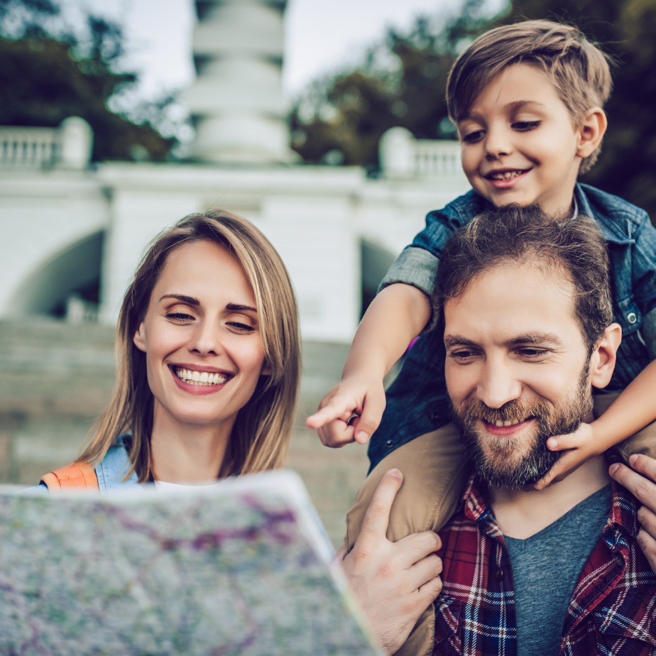 A man is carrying a child on his shoulders while looking at a map