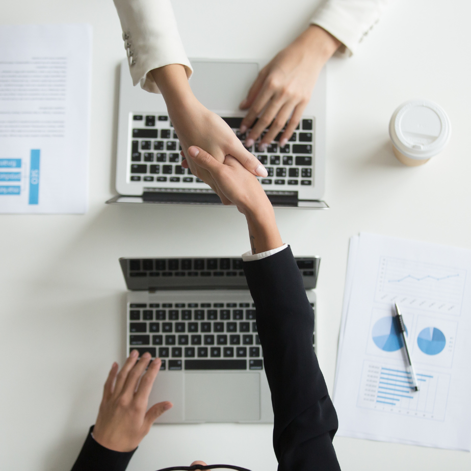 Two people shaking hands in front of a laptop