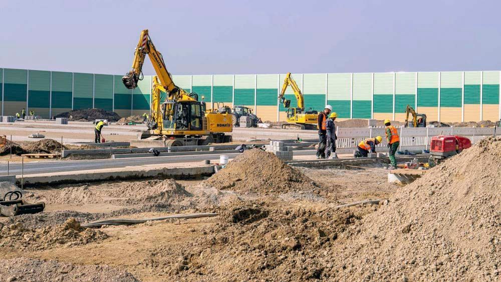 Baustelle mit Baggern, Arbeitern und einer Lärmschutzwand.