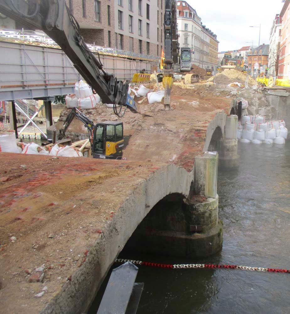 Brücke im Bau mit schweren Maschinen; Braun-, Hellbraun- und Weißtöne.