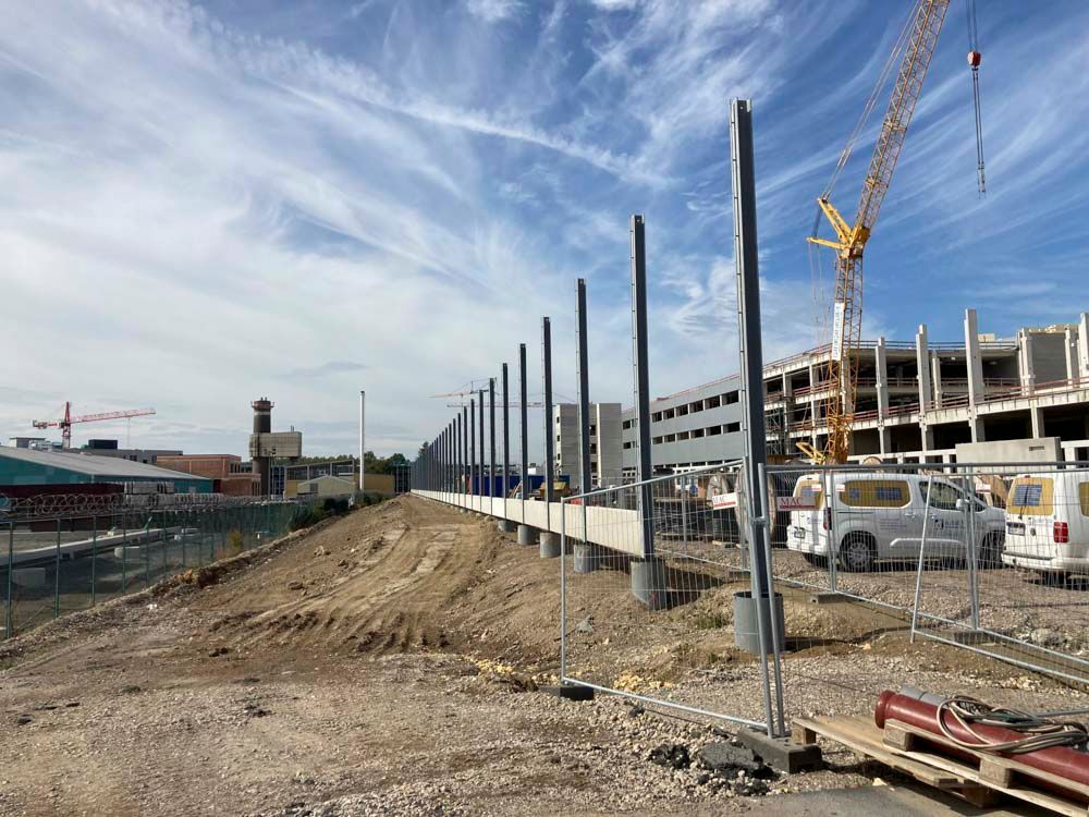 Baustelle mit Metallsäulen und einem im Bau befindlichen Gebäude. Ein Kran und Lieferwagen sind vorhanden.