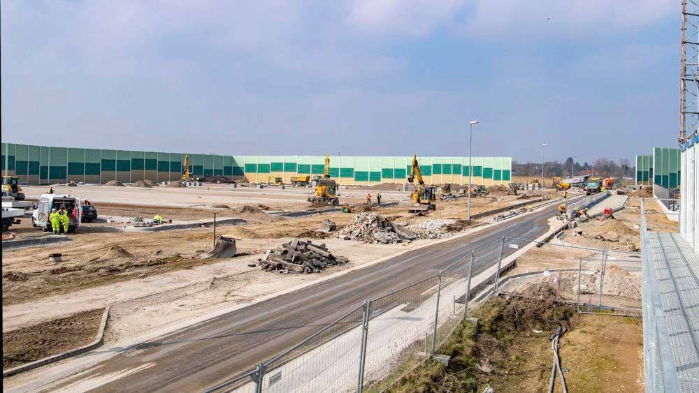 Baustelle mit Maschinen, Straße, grünen Barrieren und klarem Himmel.