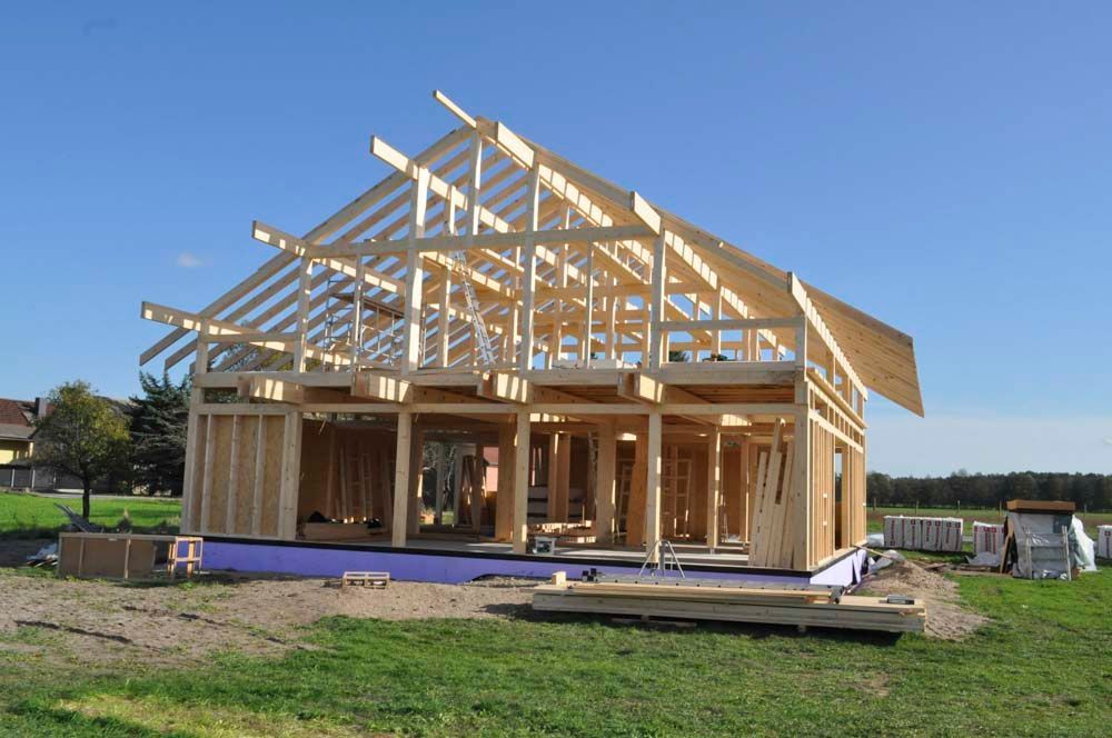 Holzhausrahmen im Bau auf einem grünen Rasen, blauer Himmel im Hintergrund.
