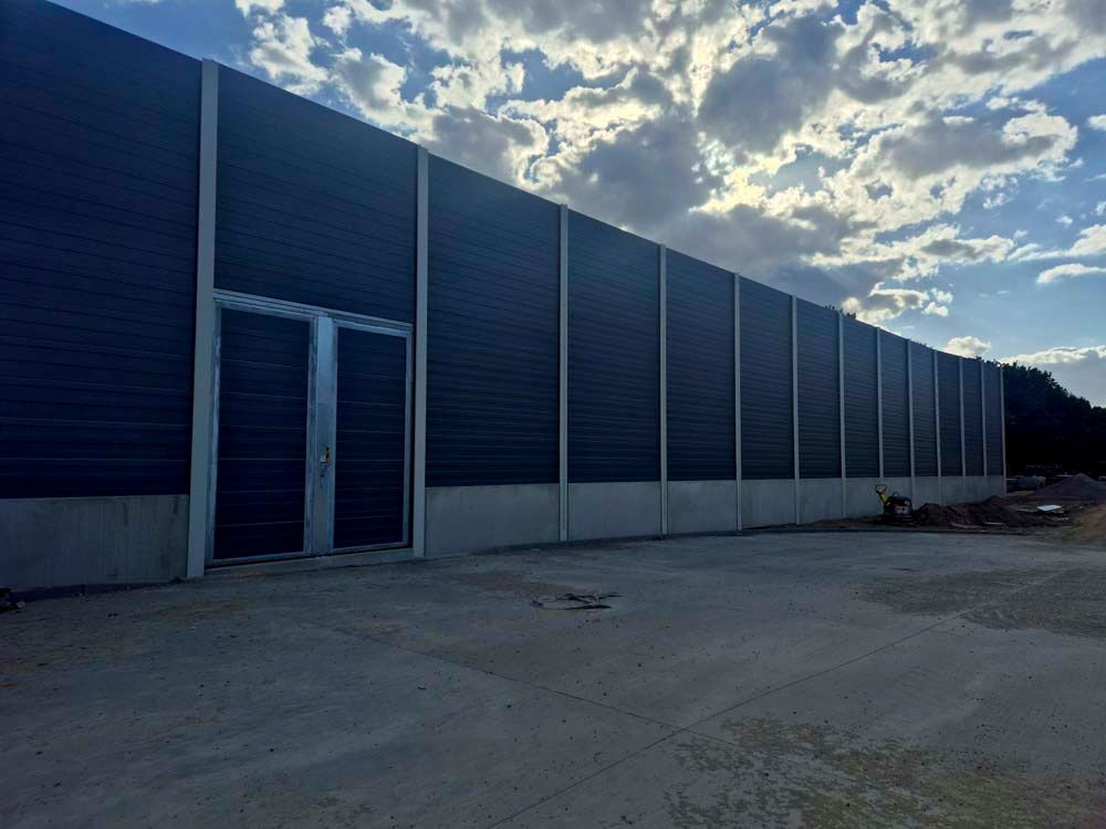 Hohe Schallschutzmauer mit Tür, bedeckter Himmel.