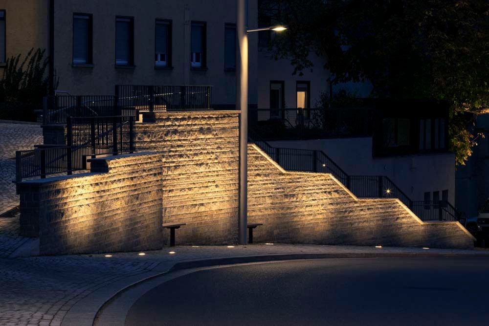 Beleuchtete Steinstufen, die nachts zu einem Gebäude führen, mit Straßenlaternen.