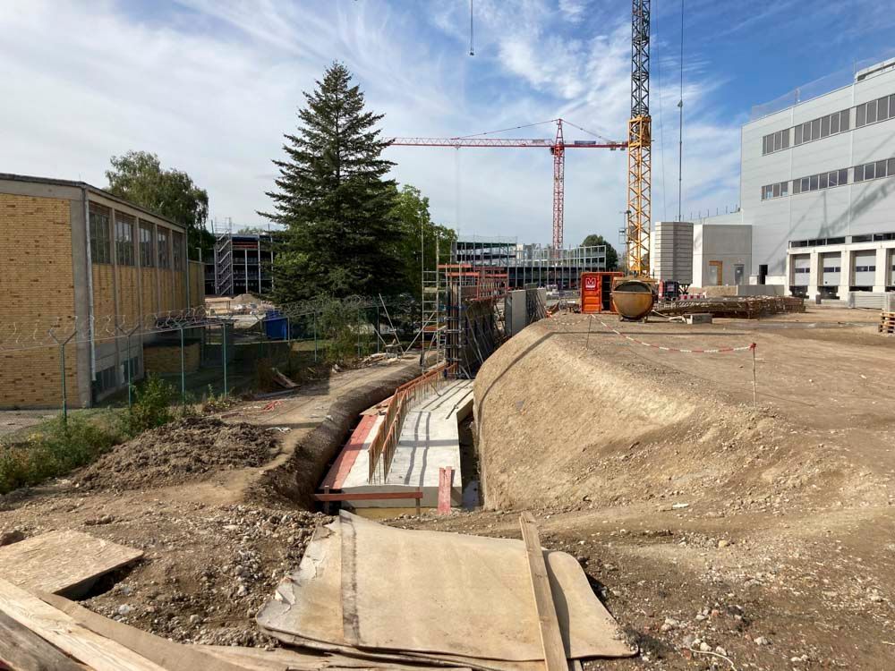 Baustelle mit Gräben, Gebäuden und Kränen unter blauem Himmel.