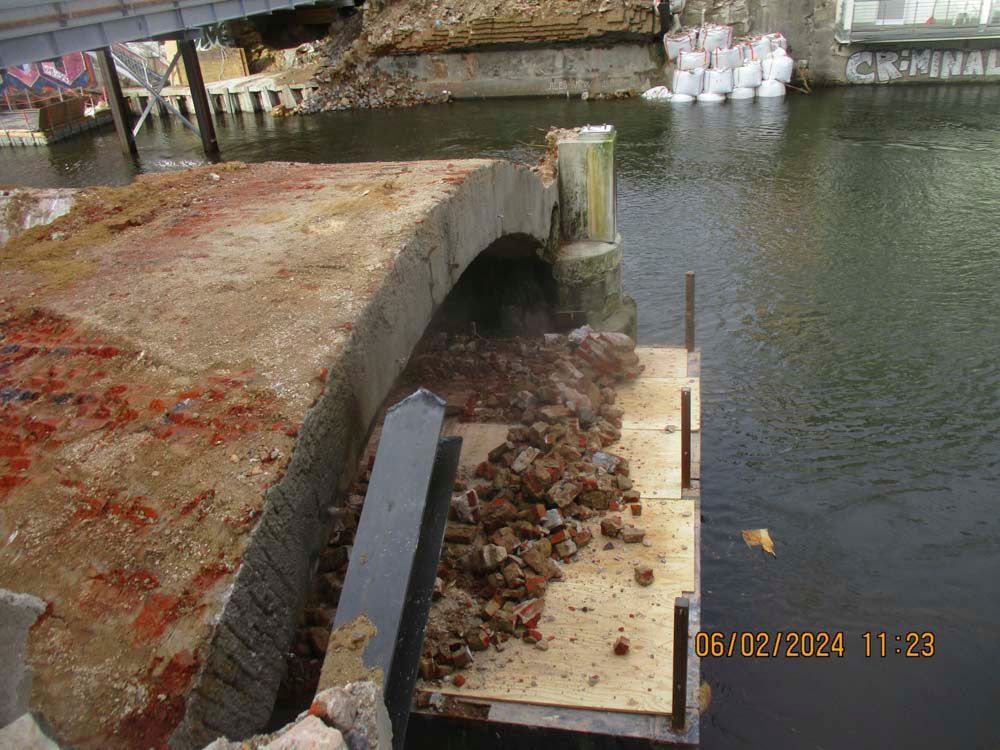 Brückenabschnitt im Bau, Trümmer ergießen sich auf eine Holzplattform über dem Wasser.