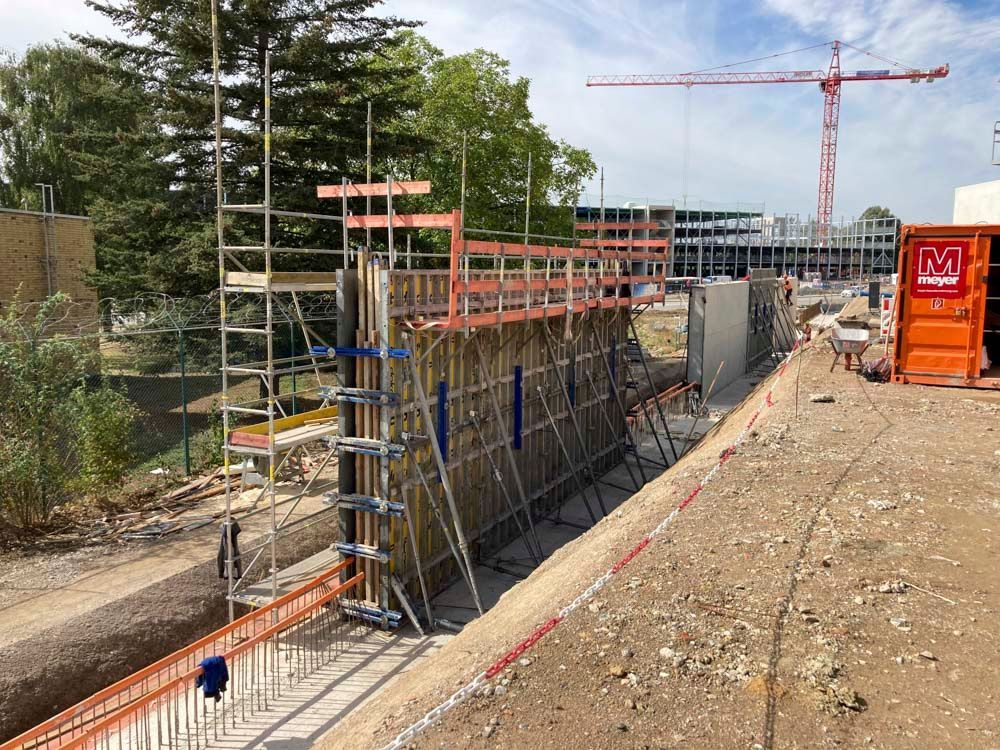 Baustelle mit Gerüst und Stützmauer, im Hintergrund orangefarbener Kran.