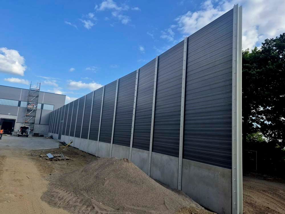 Eine lange, schwarze Schallmauer neben einem Gebäude unter blauem Himmel.