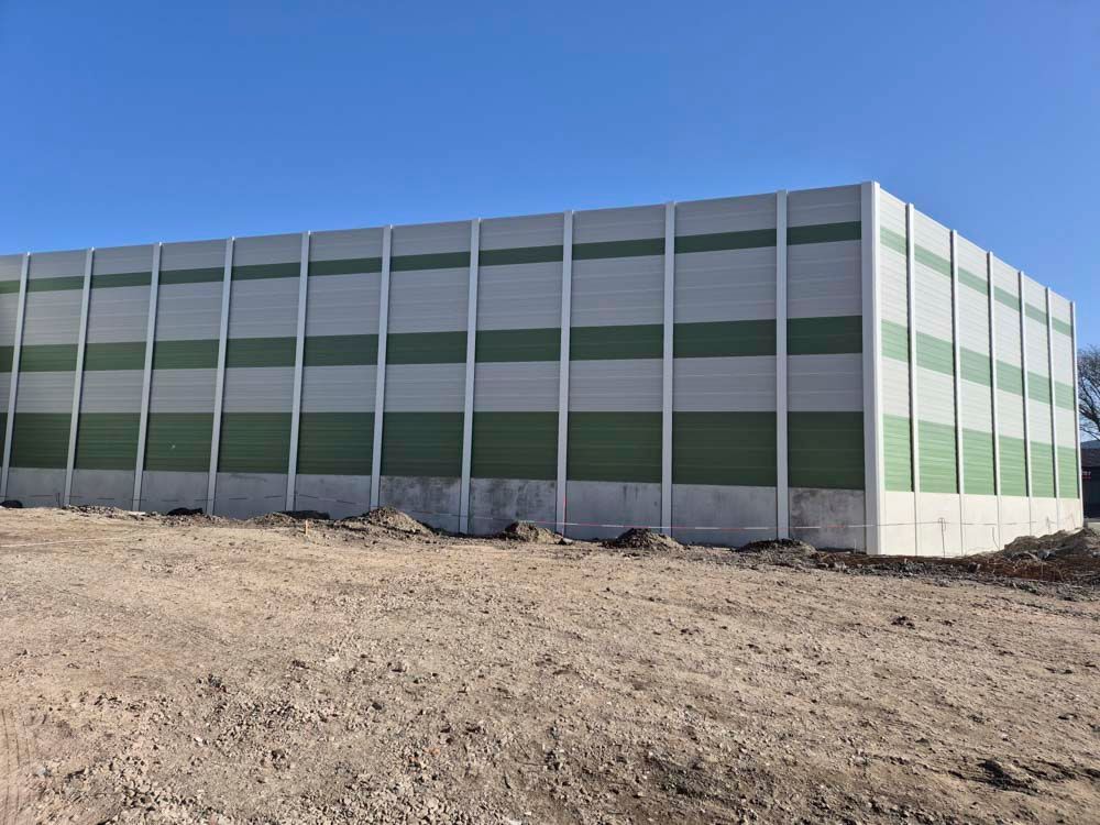 Eine lange Betonmauer mit abwechselnd grünen und grauen Streifen unter einem klaren blauen Himmel.