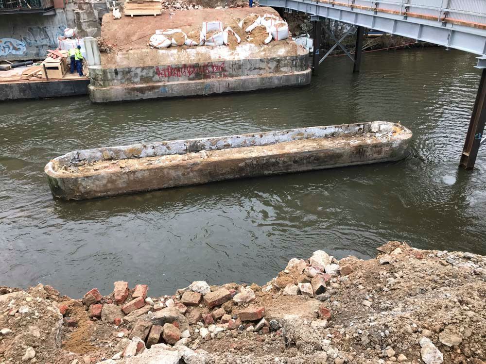 Betontrog schwimmt im Wasser unter einer Brücke. Bauschutt, Ziegel und Gebäudestützen sind vorhanden.