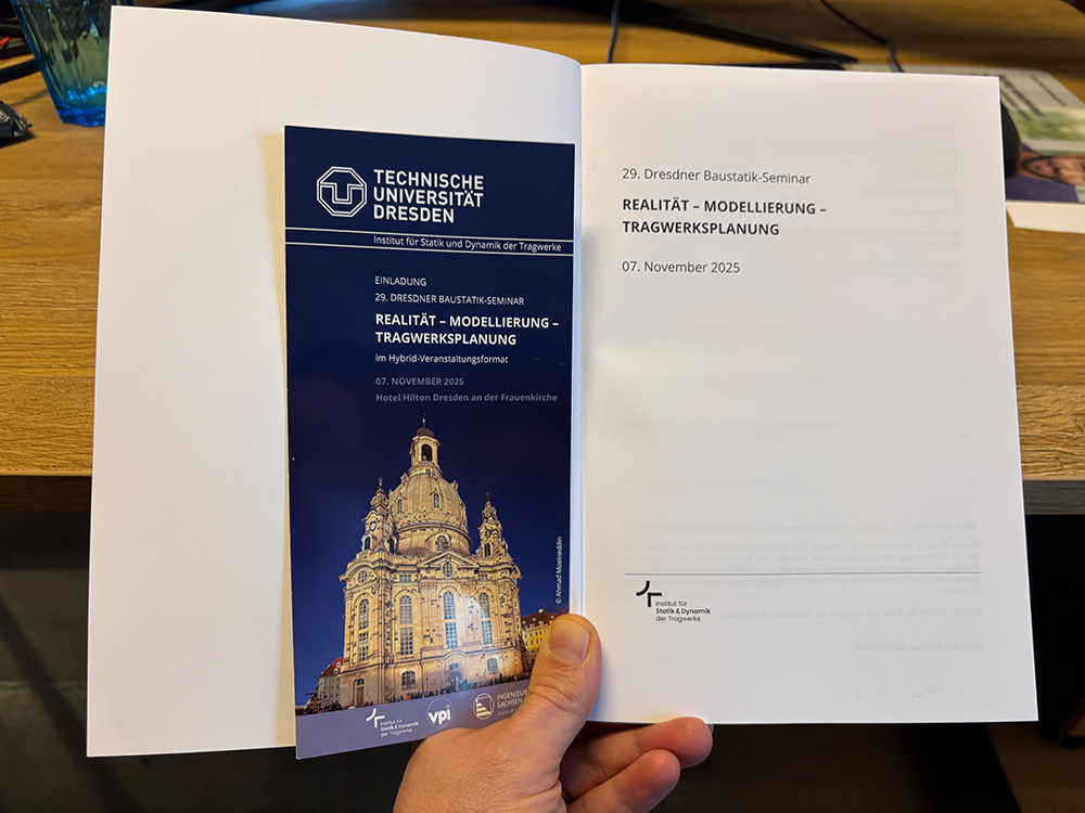 Hand holding an open document with a brochure. Brochure is dark blue with Dresden building. Text visible.