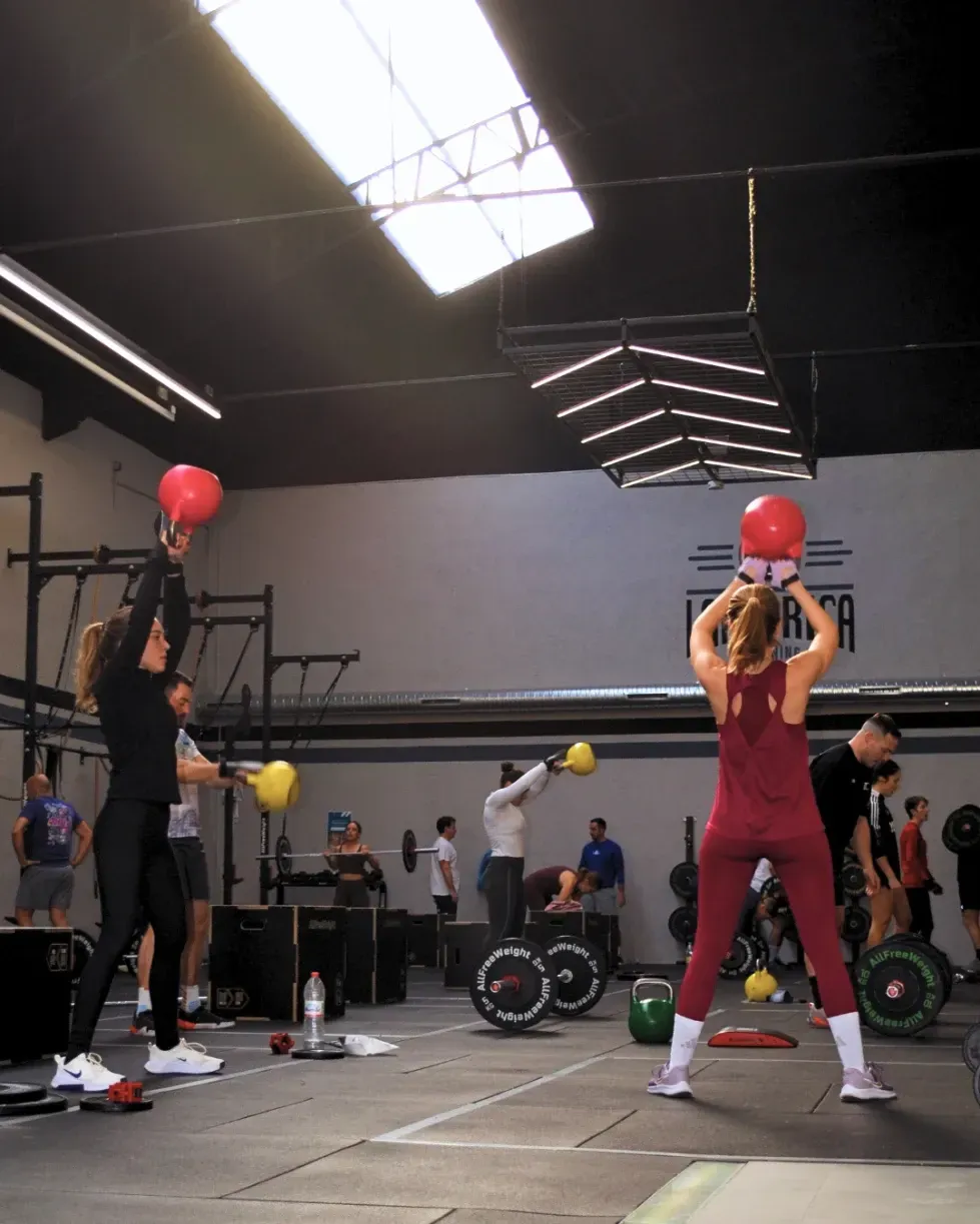 Personas haciendo ejercicio con pesas rusas en un gimnasio. Pesas rusas rojas y amarillas en lo alto.