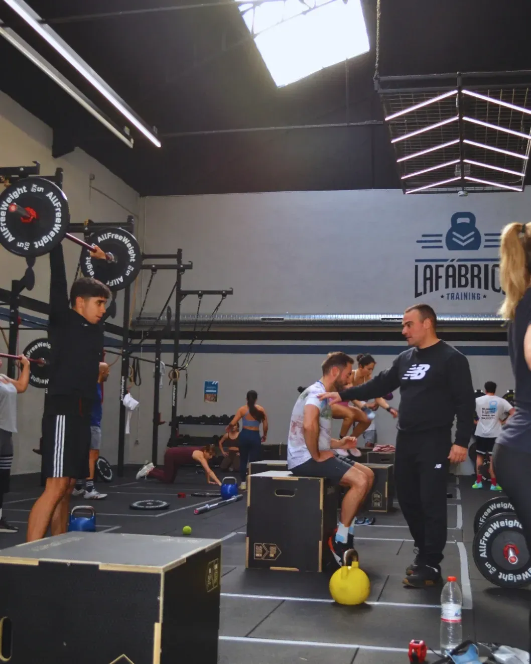 Personas haciendo ejercicio en un gimnasio con pesas, un entrenador y un logotipo.