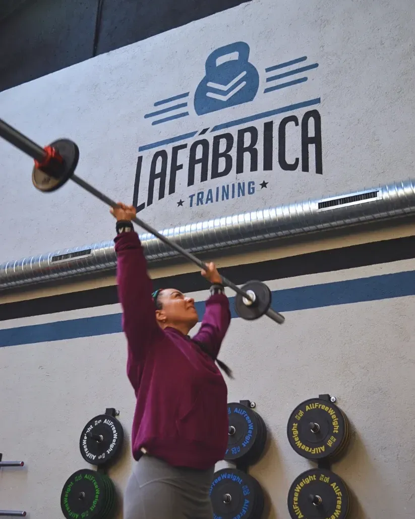 Mujer levantando una barra por encima de la cabeza en un gimnasio con el logo de 