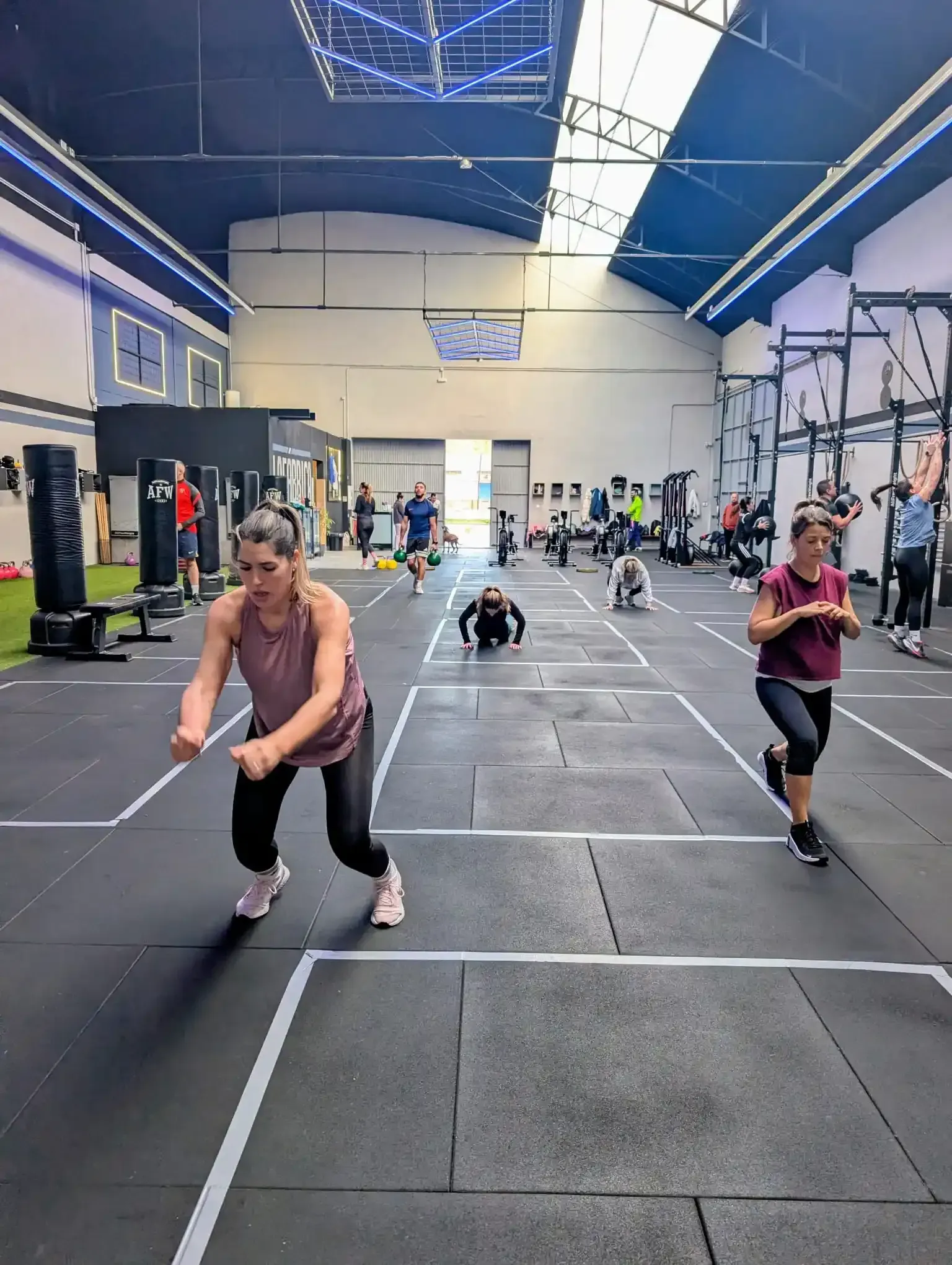 Personas haciendo ejercicio en un gimnasio con áreas de entrenamiento marcadas.