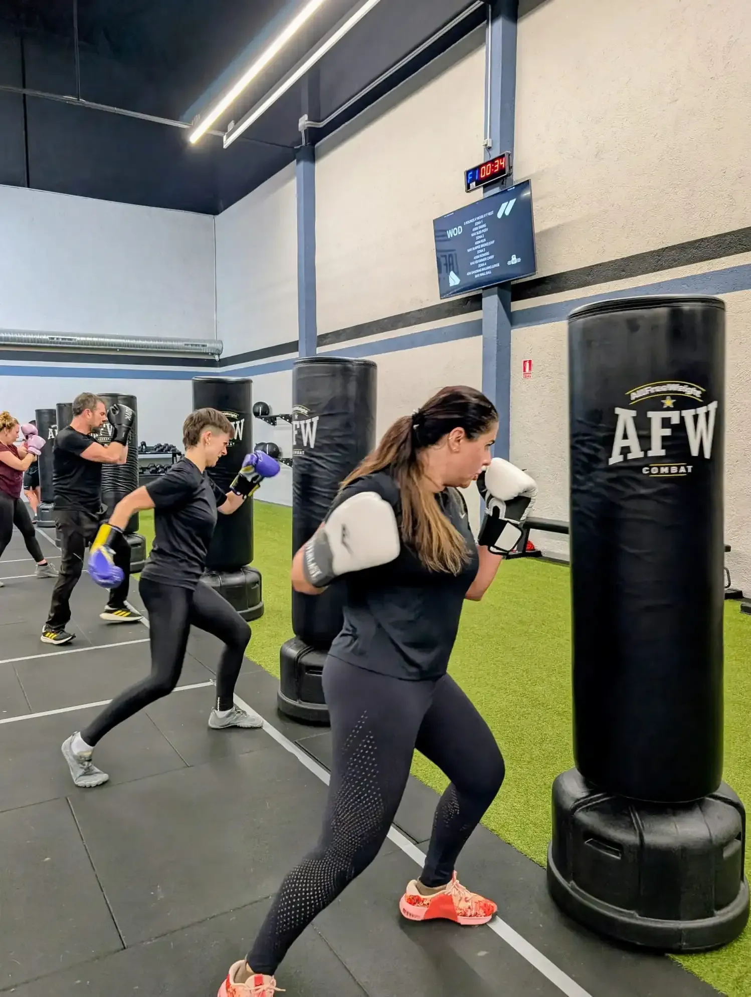 Personas haciendo ejercicio en barras de dominadas en un gimnasio; dos haciendo dominadas, uno observando.