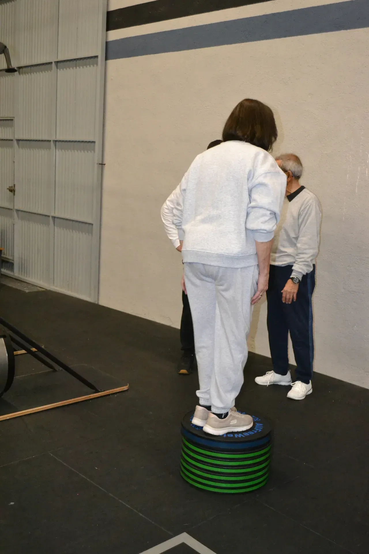 Una persona sube a una plataforma verde y negra en un gimnasio, mientras otras dos personas observan.
