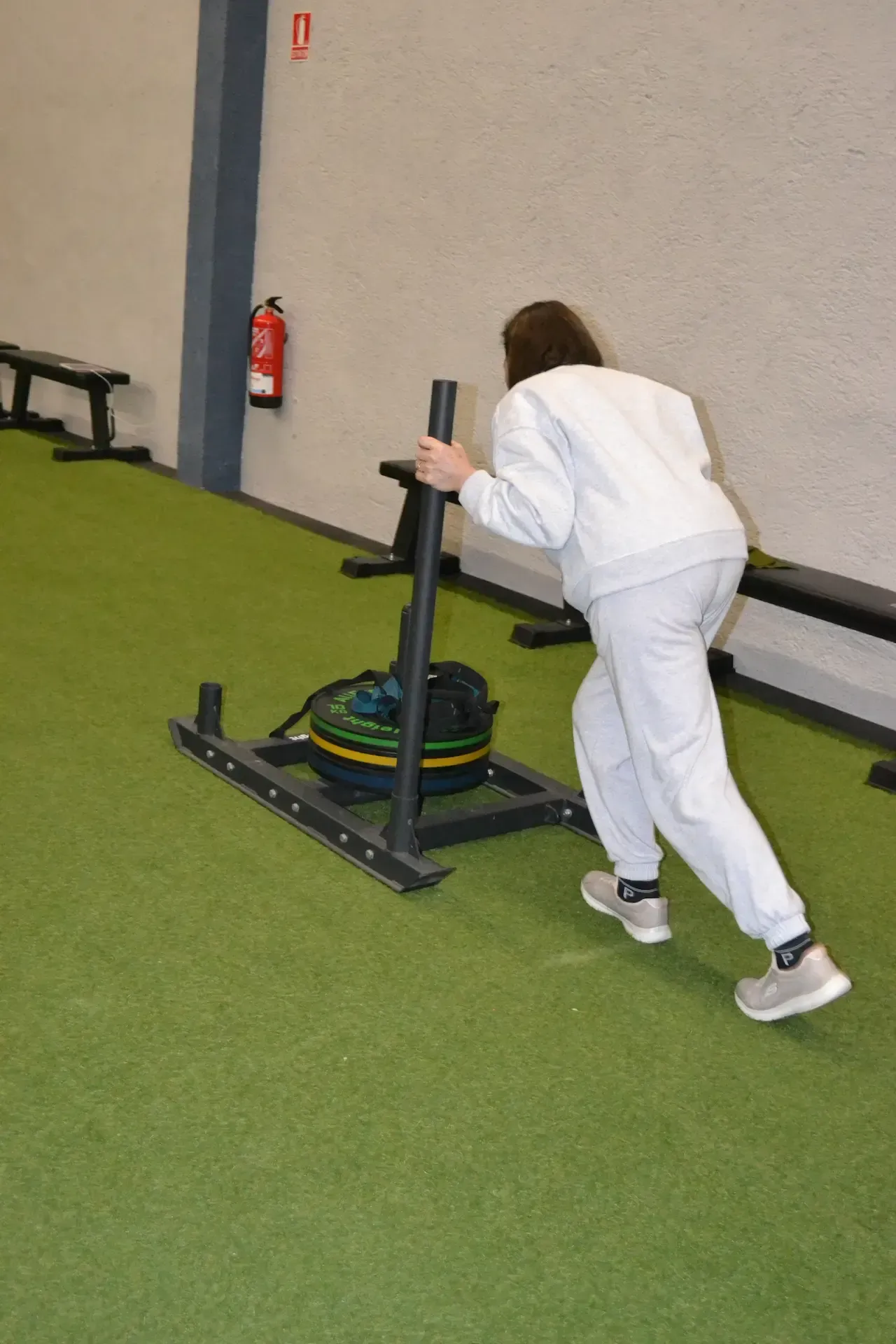 Persona empujando un trineo con peso en una pista cubierta verde.