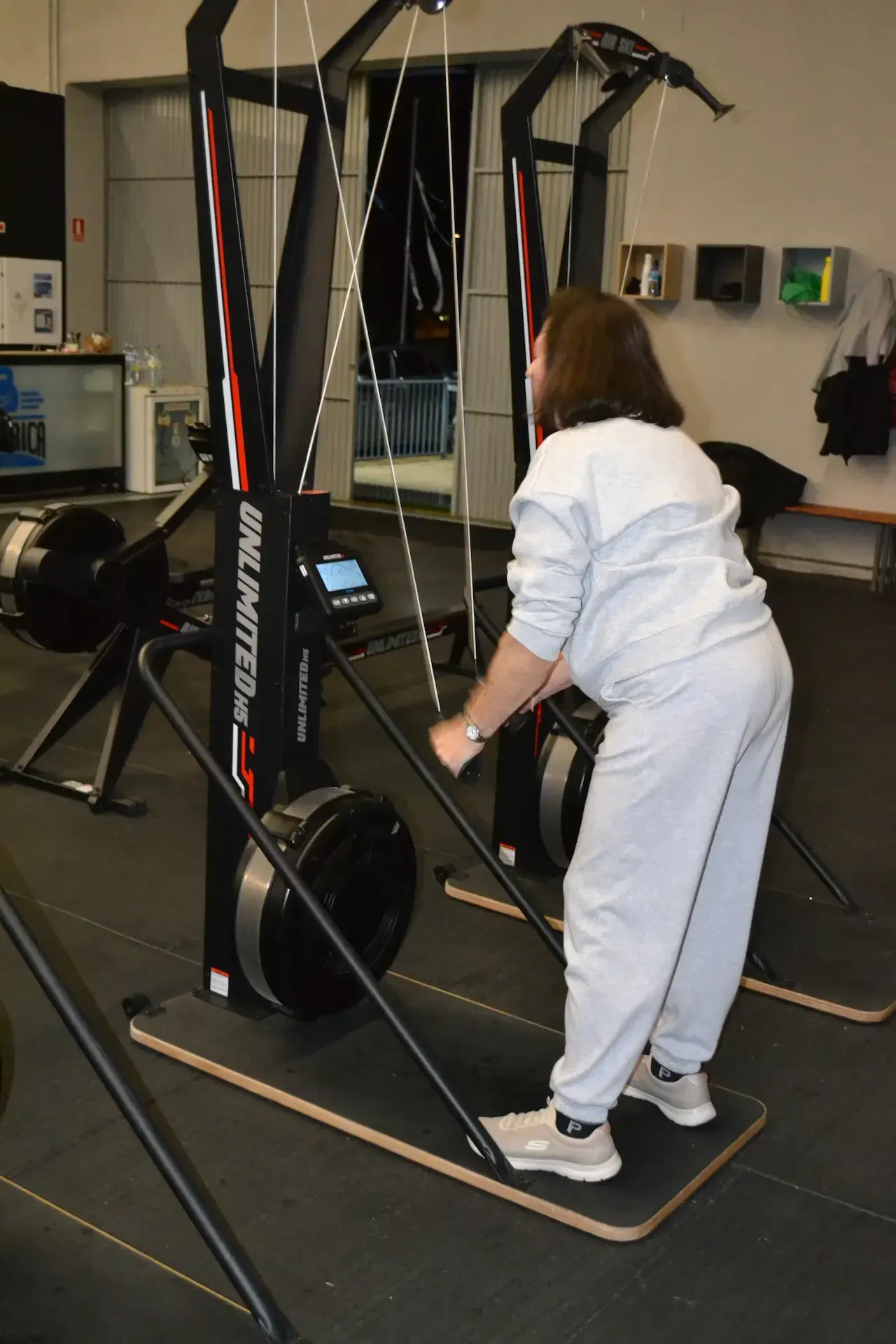 Mujer usando una máquina de skiergómetro en un gimnasio. Tira de las asas mientras está de pie sobre plataformas.
