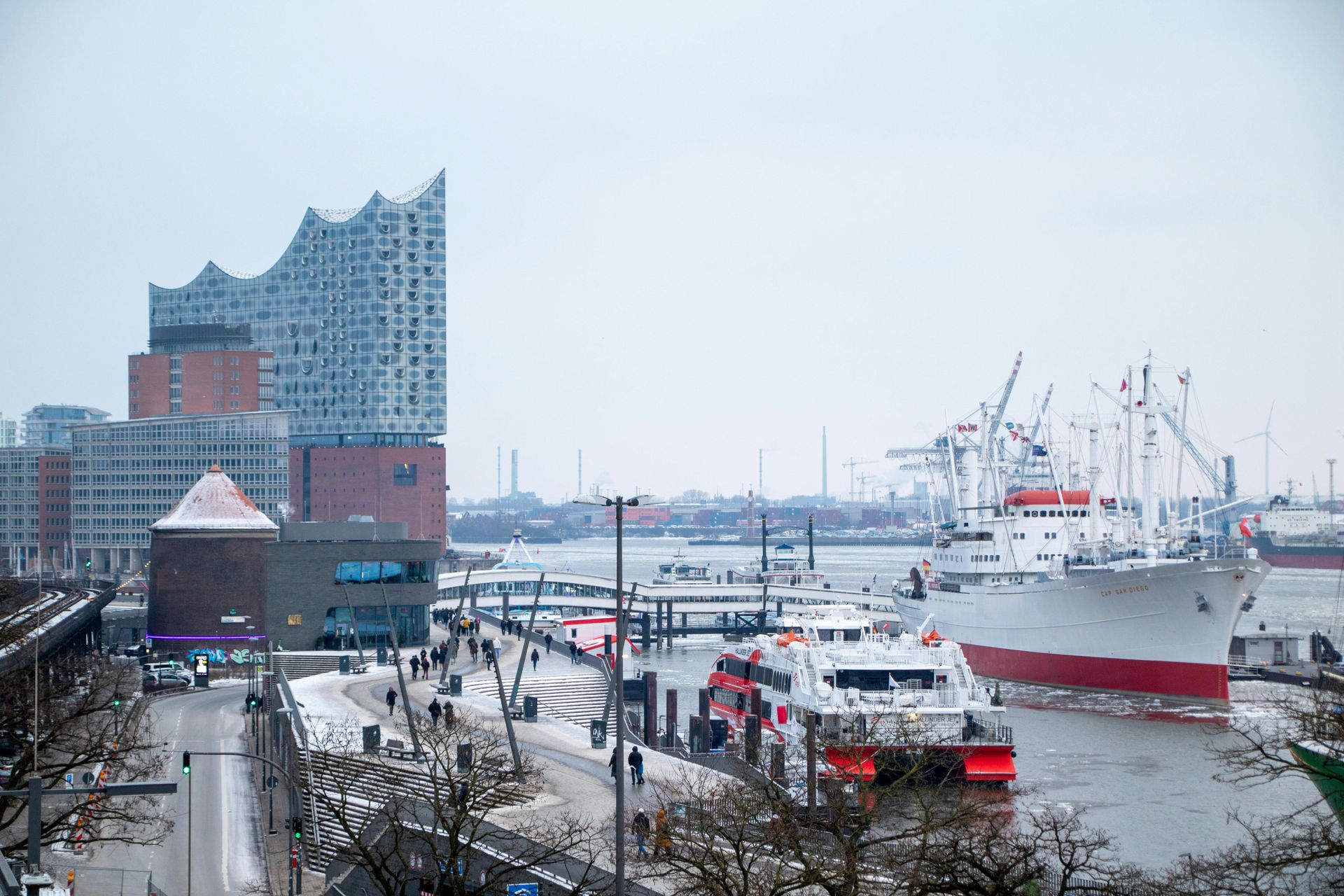 Die Elbphilharmonie thront über dem verschneiten Hamburger Hafen, in dessen eisigem Wasser große Schiffe vor Anker liegen.