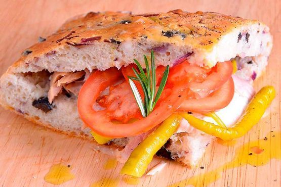 Un sándwich con tomates, pimientos, cebollas y romero sobre una mesa de madera.