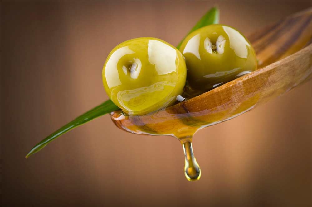Hay dos aceitunas sobre una cuchara de madera con aceite goteando de ellas.
