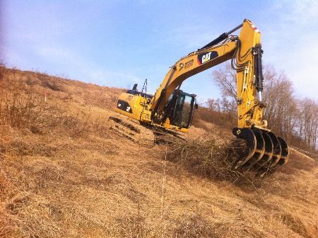 Ein gelber Bagger arbeitet an einem Hang mit trockenem Gras.