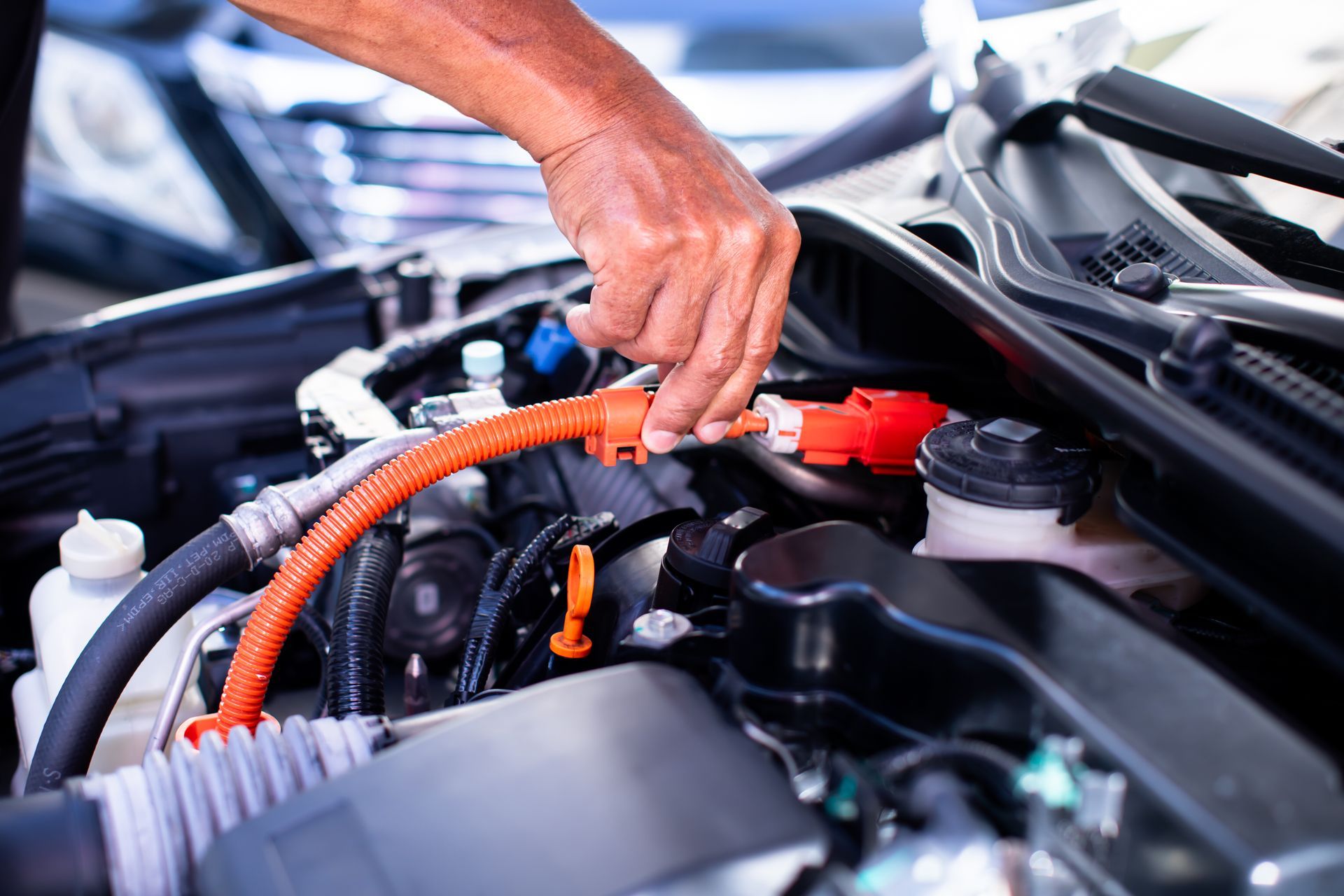 Une main branche un câble orange dans le compartiment moteur d’une voiture.