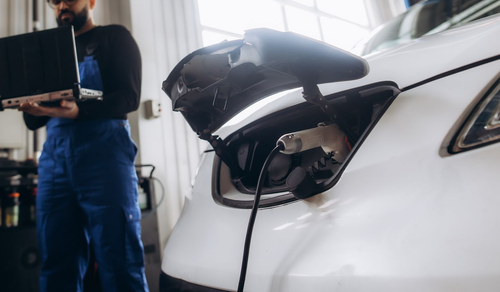 Un mécanicien recharge une voiture électrique dans un garage, avec la trappe de recharge avant ouverte et le câble branché.
